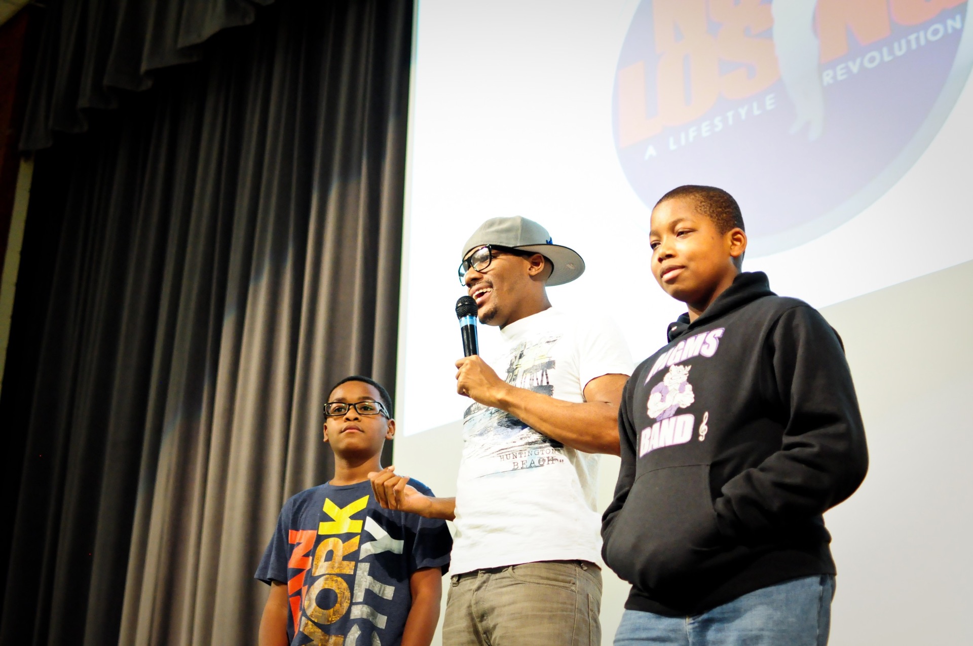 Speaker on stage with two students at a community event